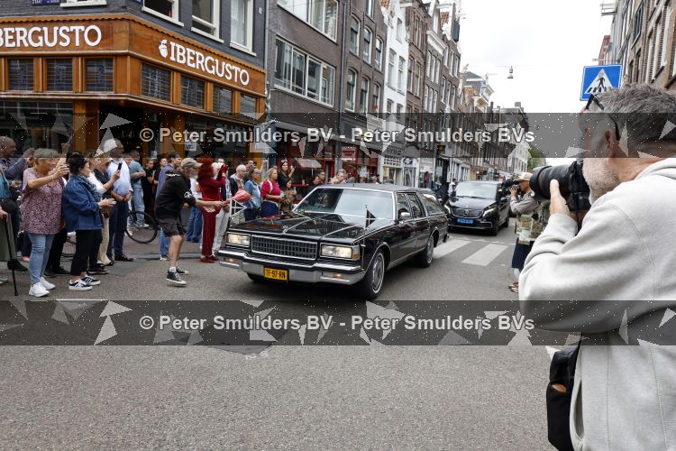 Amsterdam 17 augustus 2026
De stoet met Peter faber rijdt onder politiebegeleiding over de Haarlemmerstraat langs zijn favoriete cafe\'s . Vele mensen bewijzen hem een laatste eer.