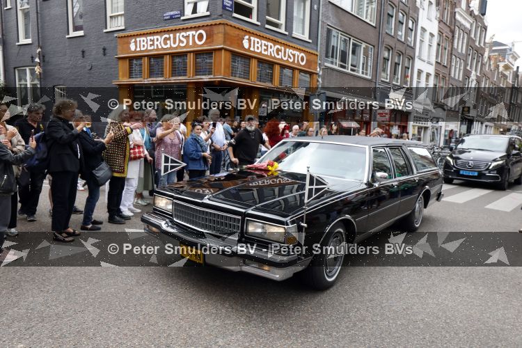 Amsterdam 17 augustus 2026
De stoet met Peter faber rijdt onder politiebegeleiding over de Haarlemmerstraat langs zijn favoriete cafe\'s . Vele mensen bewijzen hem een laatste eer.