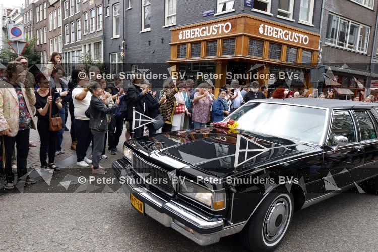 Amsterdam 17 augustus 2026
De stoet met Peter faber rijdt onder politiebegeleiding over de Haarlemmerstraat langs zijn favoriete cafe\'s . Vele mensen bewijzen hem een laatste eer.