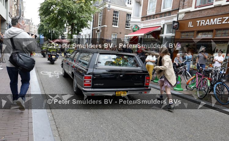 Amsterdam 17 augustus 2026
De stoet met Peter faber rijdt onder politiebegeleiding over de Haarlemmerstraat langs zijn favoriete cafe\'s . Vele mensen bewijzen hem een laatste eer.