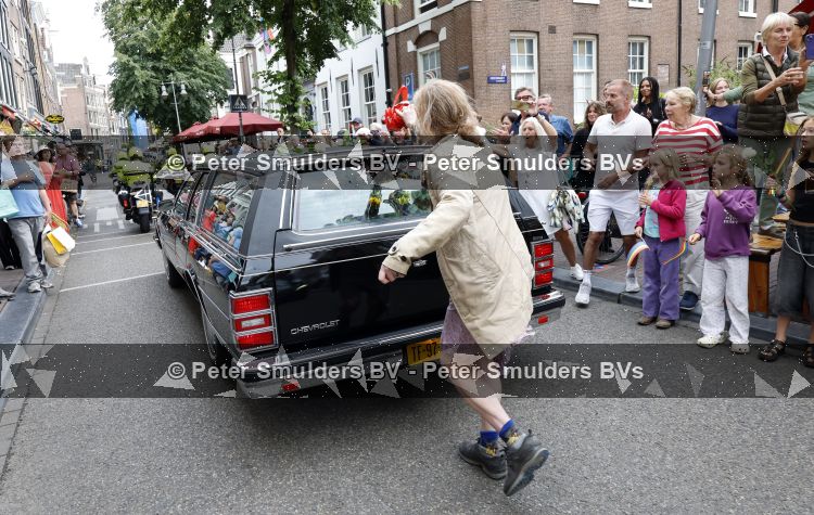 Amsterdam 17 augustus 2026
De stoet met Peter faber rijdt onder politiebegeleiding over de Haarlemmerstraat langs zijn favoriete cafe\'s . Vele mensen bewijzen hem een laatste eer.