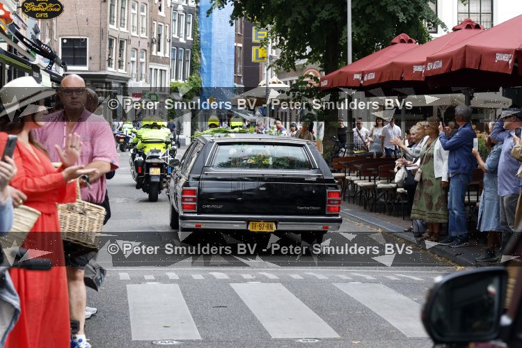 Amsterdam 17 augustus 2026
De stoet met Peter faber rijdt onder politiebegeleiding over de Haarlemmerstraat langs zijn favoriete cafe\'s . Vele mensen bewijzen hem een laatste eer.