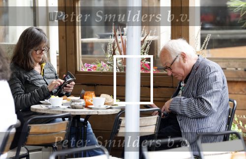 Amsterdam 1 juli 2024
Youp van t Hek en zijn vrouw Debby Petter op terras en op de fiets in Amsterdam zuid. Ze zijn beide druk op hun telefoon.